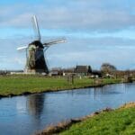 Zaanse Schans czy Kinderdijk: gdzie lepiej jechać na wiatraki? Holenderski wiatrak nad kanałem na zielonej wiejskiej łące