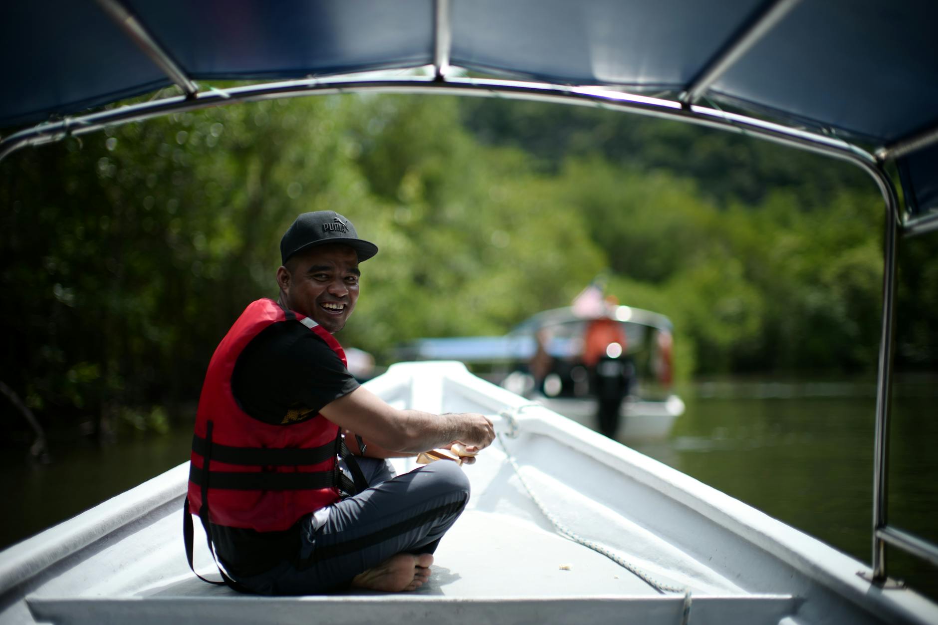 Mężczyzna w czerwonej kamizelce płynie łodzią po zielonej rzece