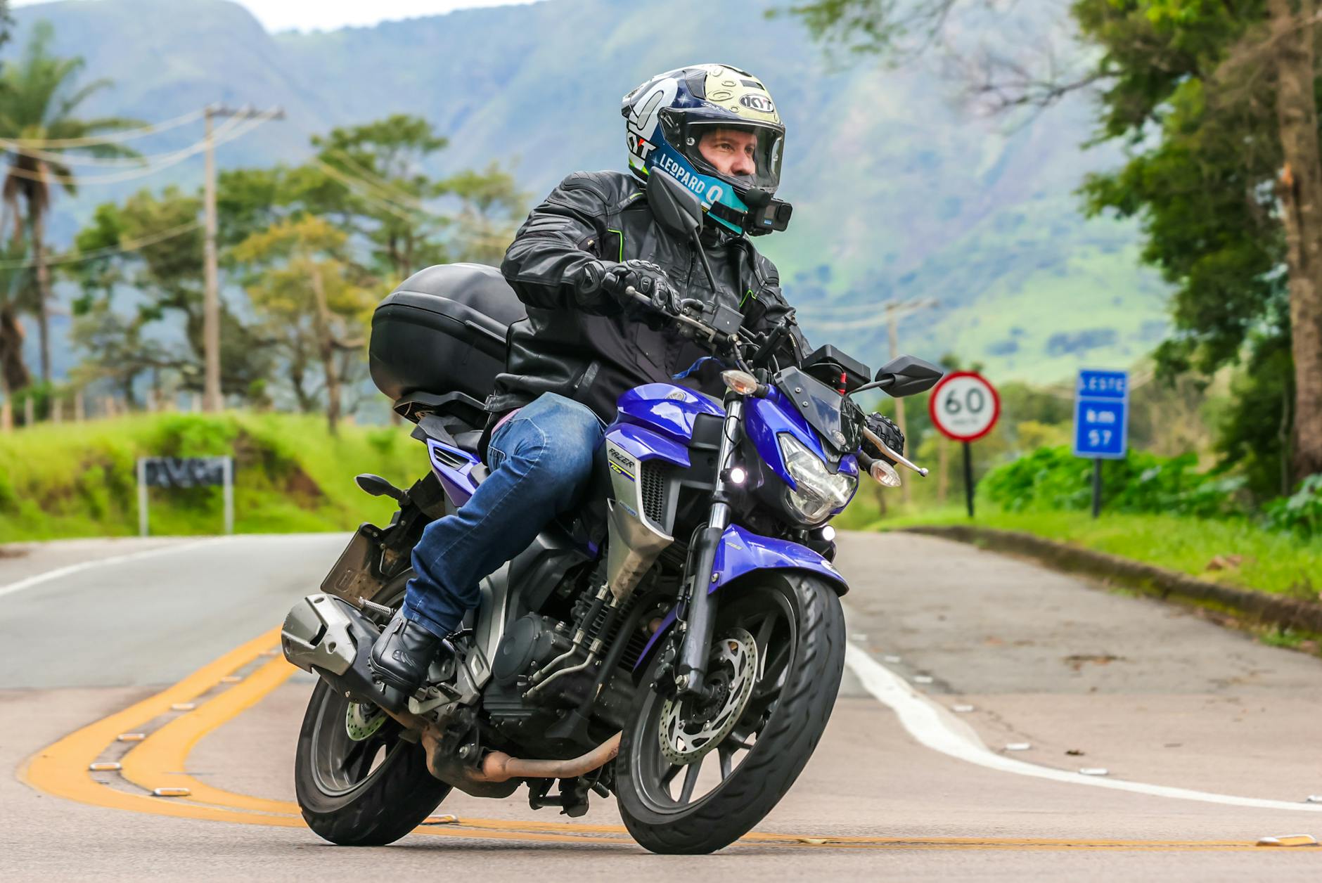 Motocyklista na niebieskim motocyklu jedzie malowniczą szosą