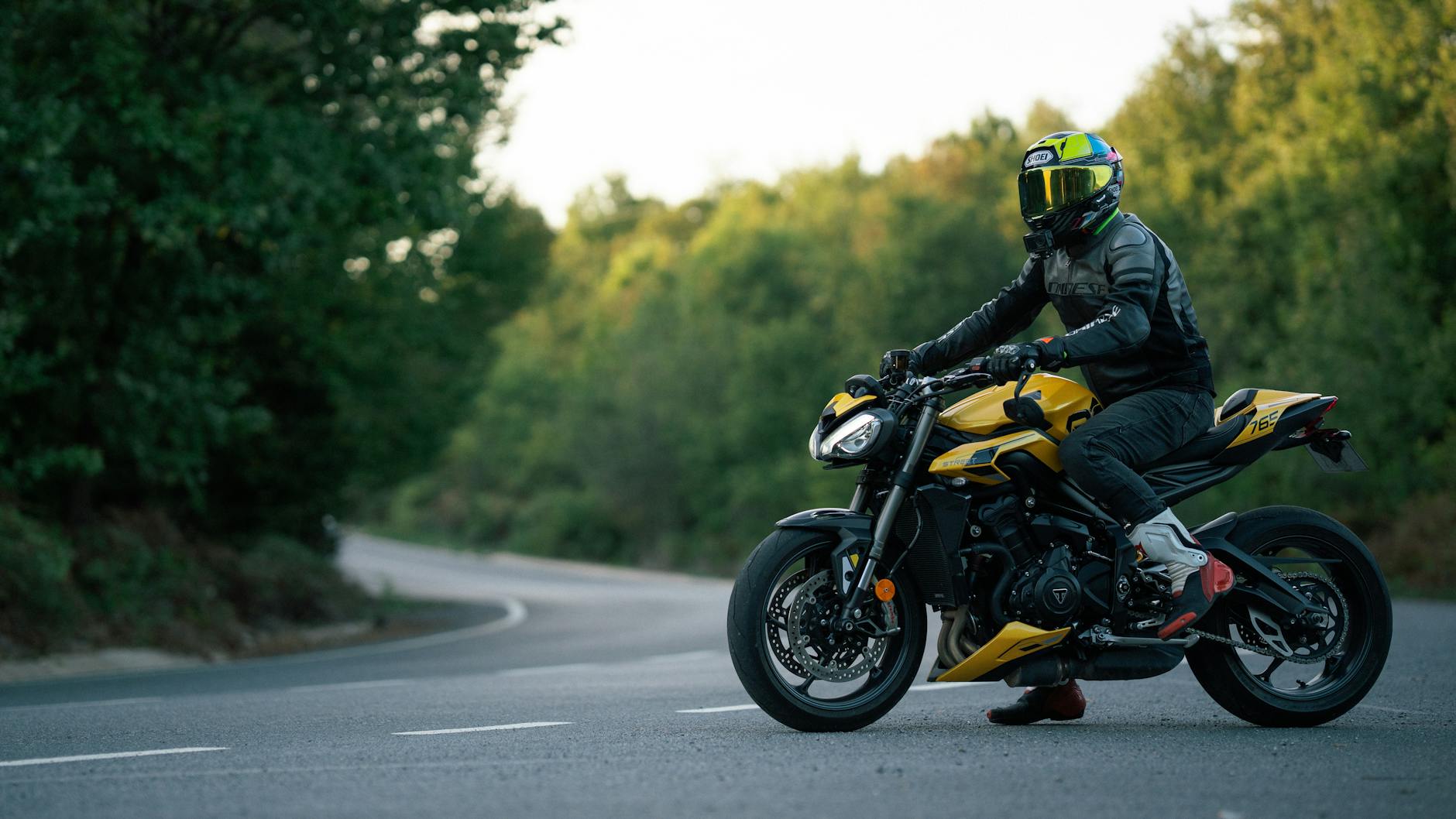 Motocyklista na żółtym sportowym motocyklu jedzie leśną szosą