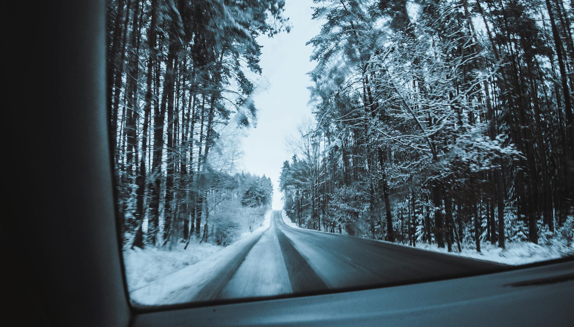 Zimowa droga przez ośnieżony las widziana z okna jadącego auta