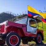 Stary jeep Willys z flagą Kolumbii na tle zielonej wiejskiej okolicy
